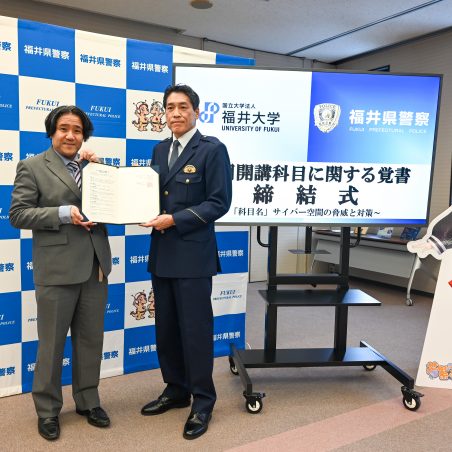 締結した覚書を手に並ぶ、岸教授と福井県警察生活安全部長北道貞邦氏